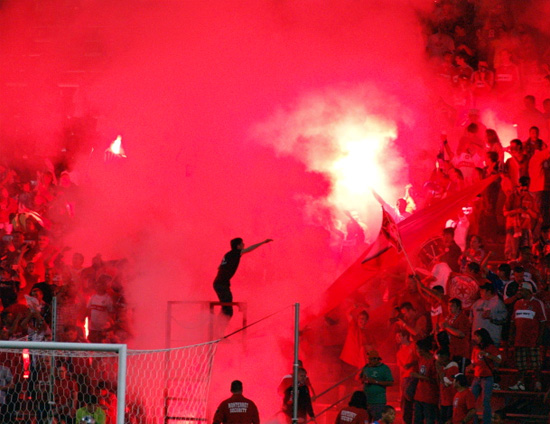 section8-capo From afar, the silhouhette of the capo in front of the pit of flames and smoke gave him a spectral presence, as he bounced on the stand, the roar now spreading all around the stadium.